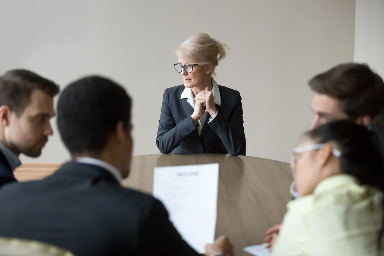 A person being excluded from a conversation around a boardroom table.