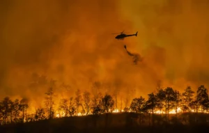 A helicopter dropping water over a wildfire.