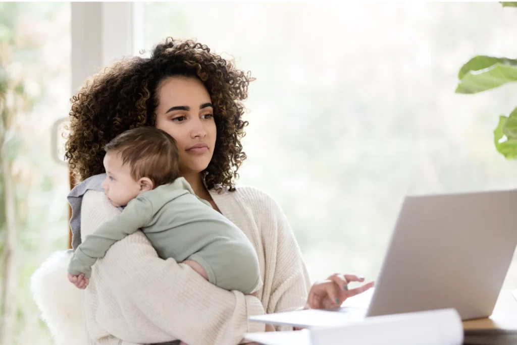 Woman working remotely while holding a baby.